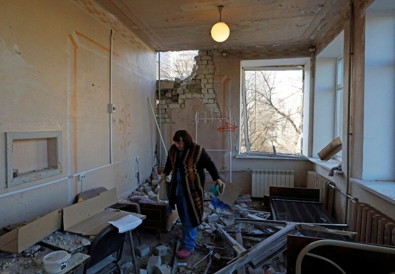 A woman picks up debris inside a building, surrounded by pieces of concrete and a damaged window.