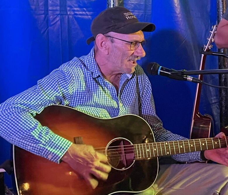 A man sits playing guitar and singing into a microphone. 