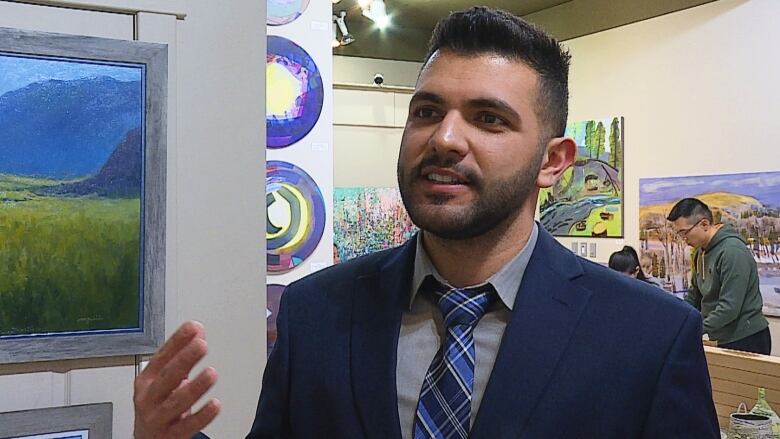 A man in a blue suit speaks to a reporter at an art gallery.