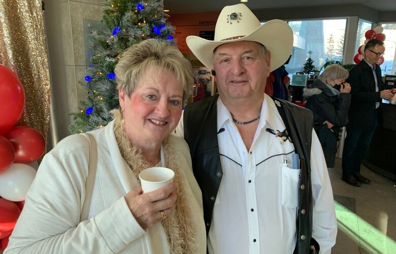 A man and a woman stand together holding coffee.