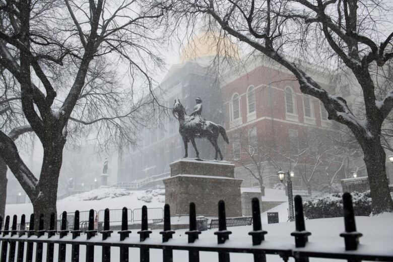 A statue of a person on a horse with snow falling in front of Massachusetts State House.