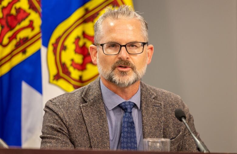 A man with glasses and a beard smiles while listening to questions.