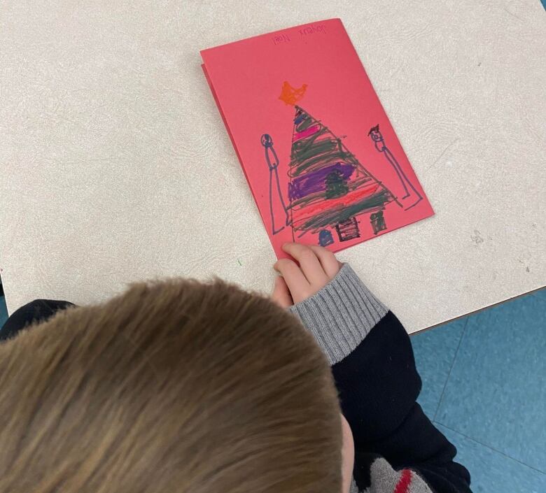 The top view of a child's head beside a hand-drawn card on red craft paper