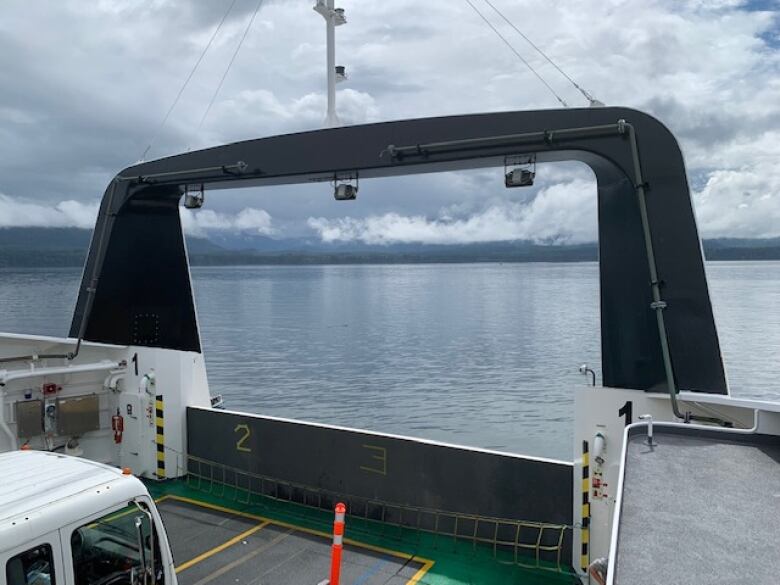 The front of a small car ferry overlooks the ocean with land in the near distance. 