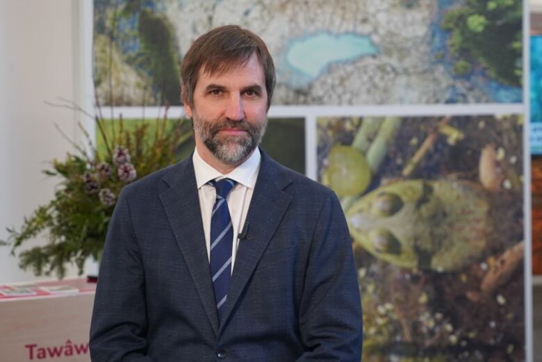 A man wearing a blue suit with a white shirt and blue tie with a grey diagonal stripe poses for a photo.