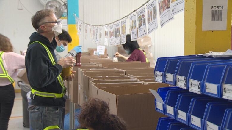 A man with a can of non-perishable food looks at some fliers above a line of boxes.