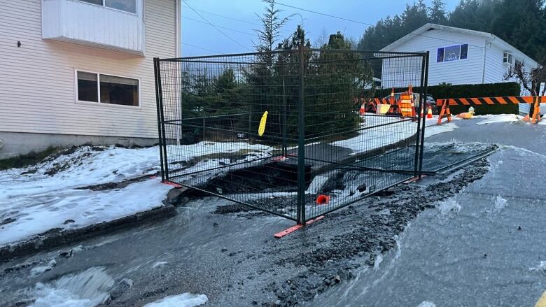 Metal fencing surrounds a section of crumbling asphalt as water pours out of a broken pipe.