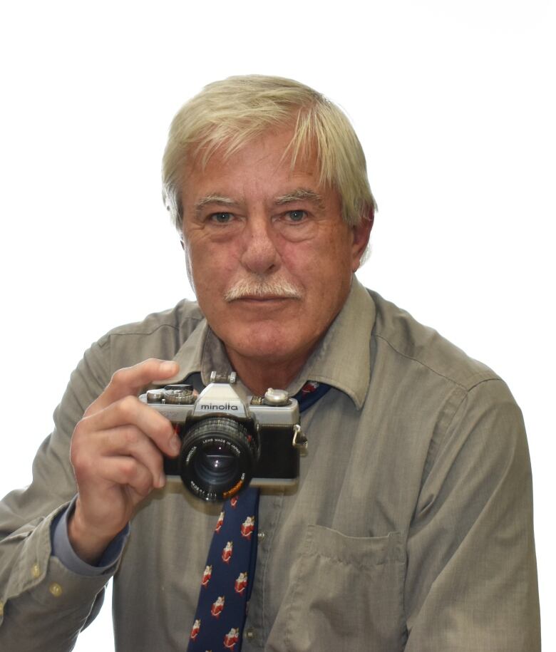 A man in a  brown shirt with blonde hair holding a thirty year old camera. 