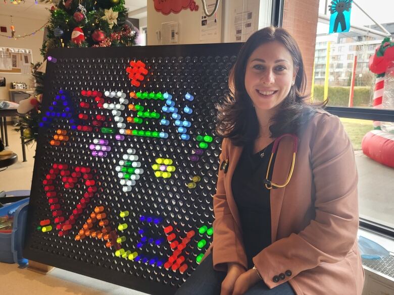 A woman smiling next to a giant Lite-Brite toy. 