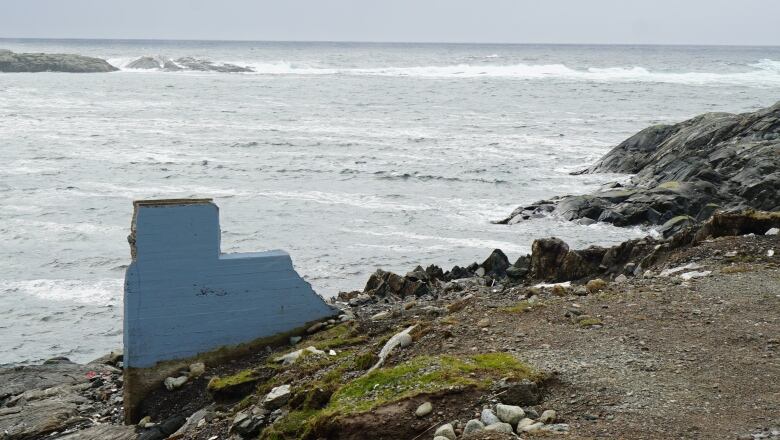 A small L-shaped wall stand in the dirt with the ocean in the background. 