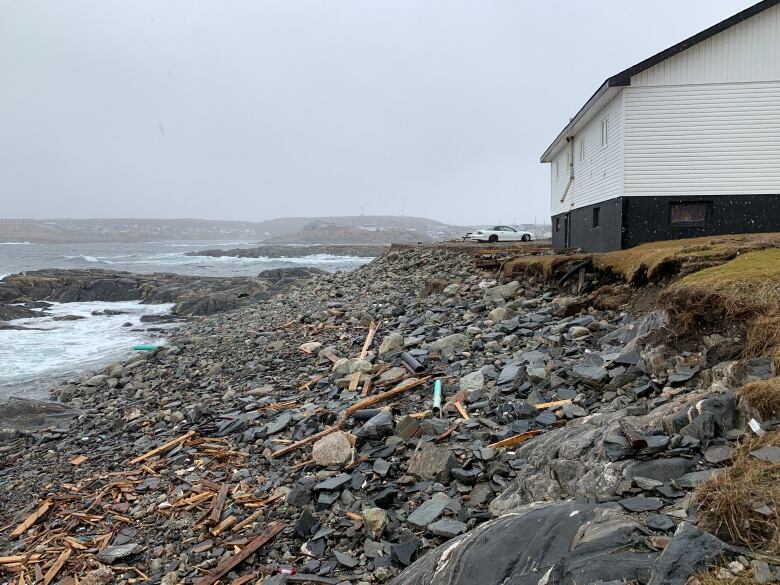 A pile of rocks separates a white house from the ocean 