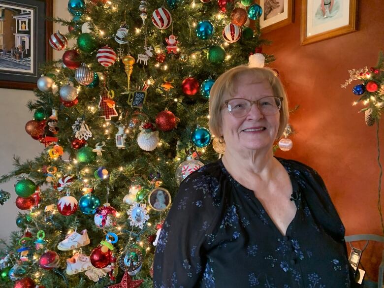 Dorothy Bragg stands in front of a large Christmas tree decorated with various ornaments. 