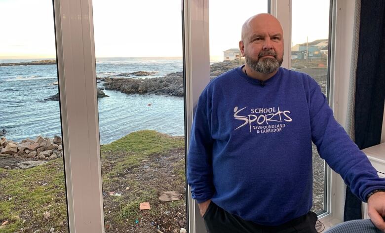 Scott Strickland stands in front of a large window, with the sunsetting on the ocean in the back.