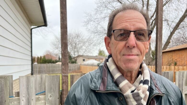 A man with glasses stands in front of a fence.