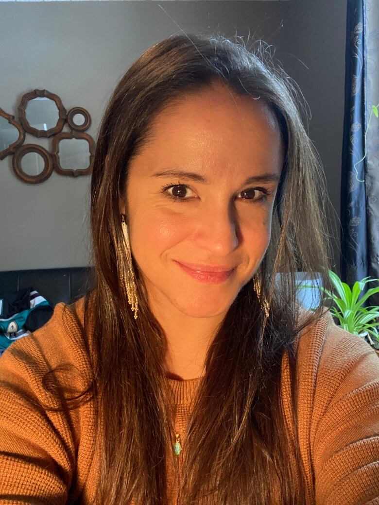 Robin Paul is an Indigenous artist wearing gold earrings, brown hair and an orange top