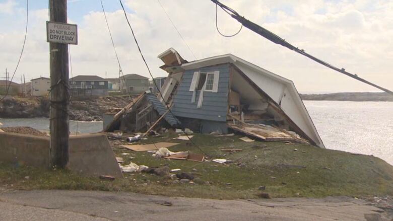 A damaged blue home collapsed on its side. 