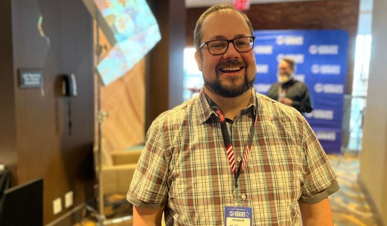 Jeff Clemens laughs as the photo is taken. He is wearing a plaid t-shirt sleeve button up. His glasses are thicker and darker-rimmed. His beard and moustache are kept short. 