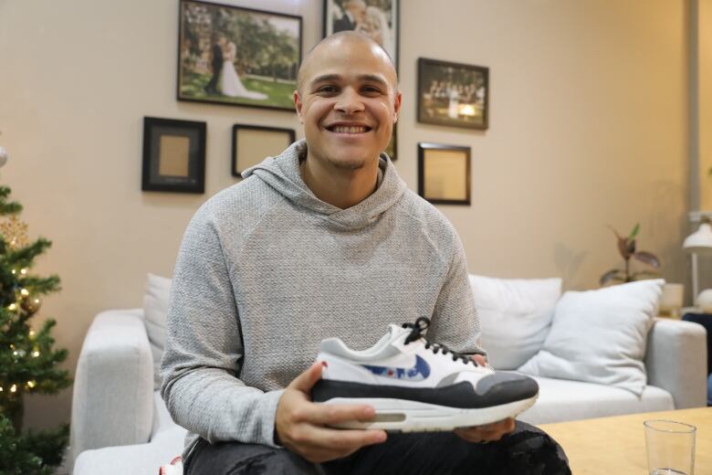 A young man sits holding a sneaker and smiling. It has an ajnime character painted inside the Nike swoosh. 