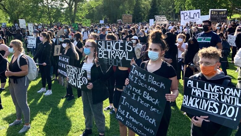 A large crowd of people, many of them holding protest signs with words like Black Lives Matter and Silence is Betrayal.