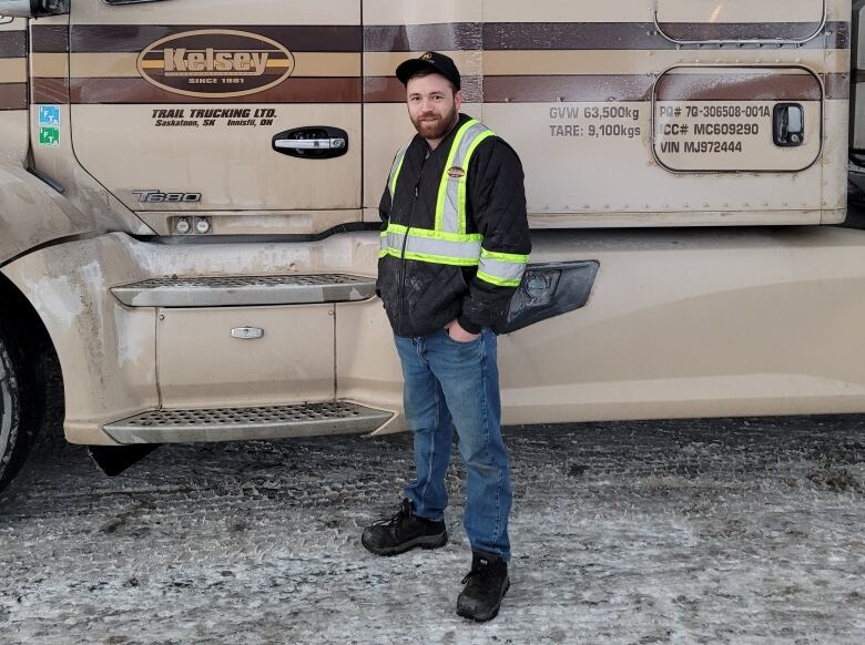 A man stands in front of a parked semi-truck in a parking lot. 