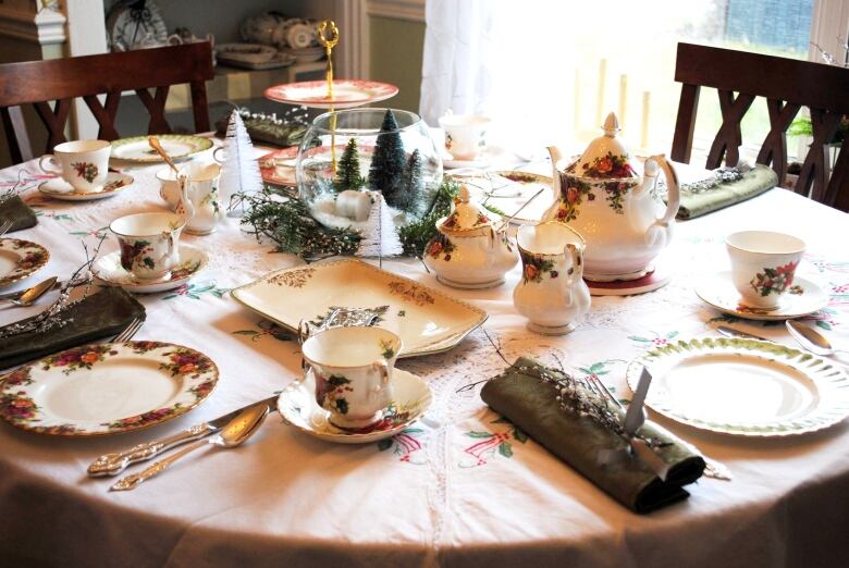 A dining table is set with various china tea cups, saucers and teapots.