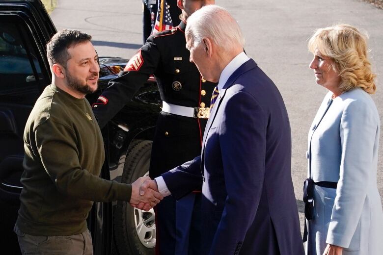 Individual in green chamo type clothing stepping out of a limo and shaking the hand of the U.S. president, as the president's wife looks on. 