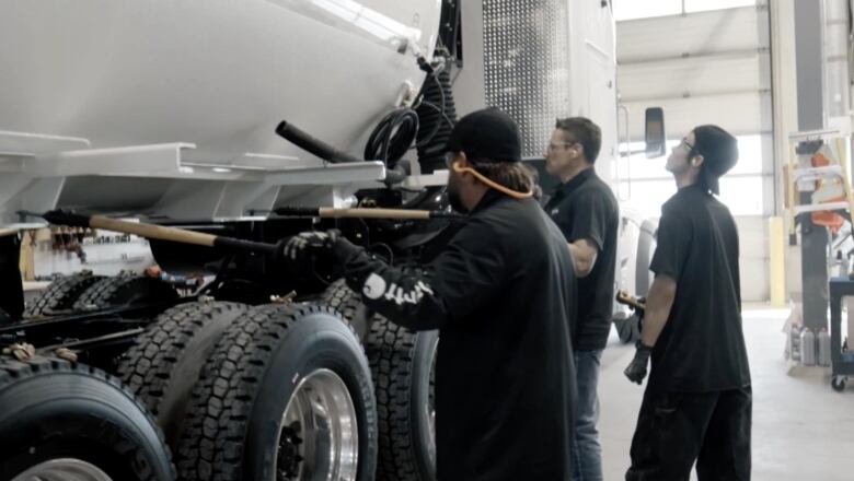 Three employees of Tornado Global Hydrovacs stand next to a truck that is being assembled in Red Deer, Alta. 