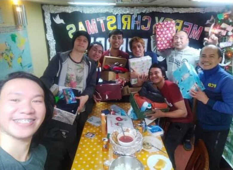 A group of seafarers are smiling at the camera holding opened care packages.