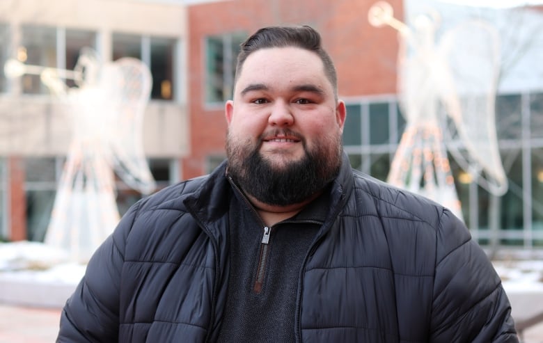 A man in a winter coat stands outside smiling at the camera. 