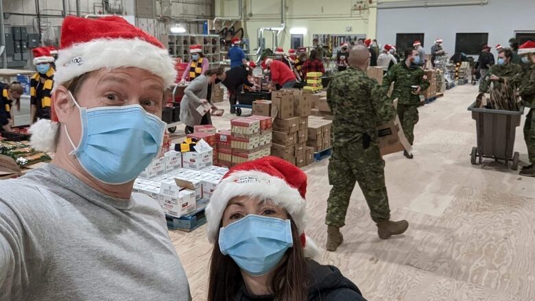 Geoff Richardson and Tracy Sloan wearing face masks and santa hants, with people filling boxes in the background. 