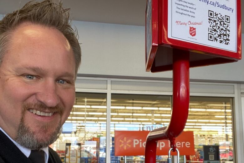 Close up photo of Jeff Robertson smiling next to a red Salvation Army Christmas kettle. 