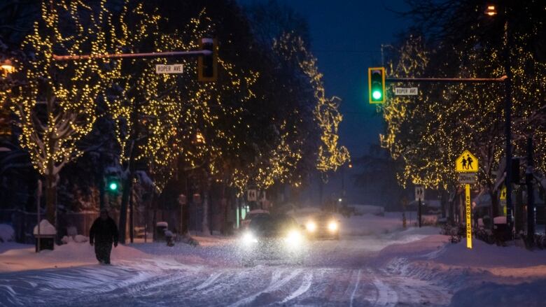 Two cars follow each other, headlights on in the dark as snow falls