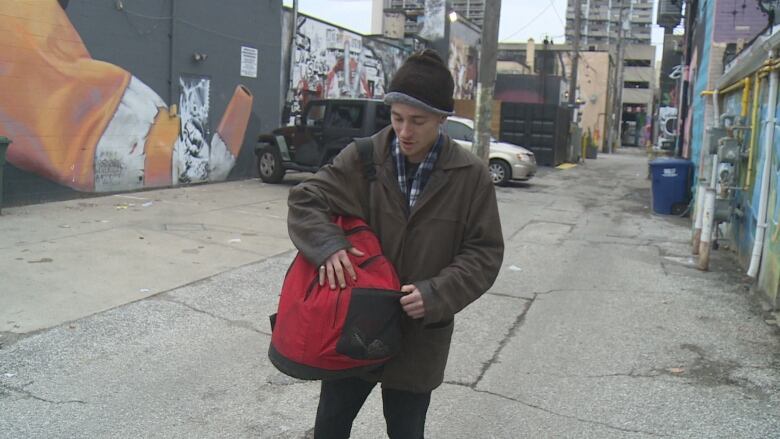 Man walking in downtown alley holding his red backpack.