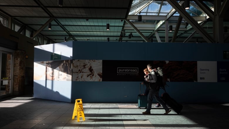 Two travellers with rolling suitcases are pictured walking past an area under construction at Vancouver International Airport.