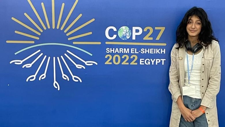 A teenage girl standing next to a wall that says COP 27.