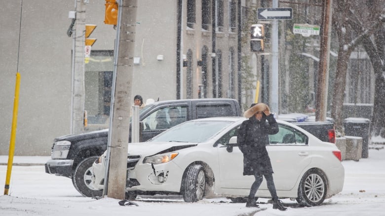 A person walks past a car that crashed into a nearby electricity pole.