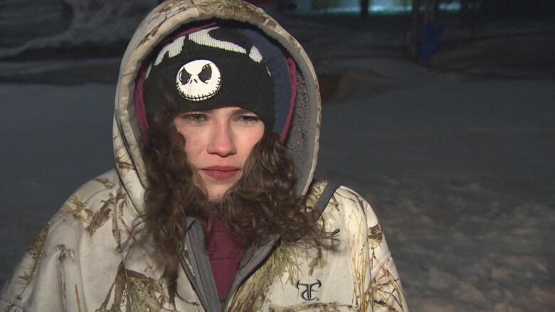 A woman in a cream coloured jacket stands outside in the winter cold.