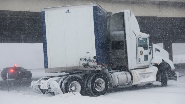 A jackknifed transport truck under an overpass on a snowy road.