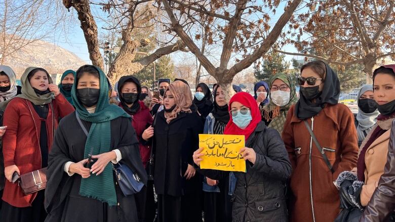 A group of women gather outside, one holding a sign with writing on it.