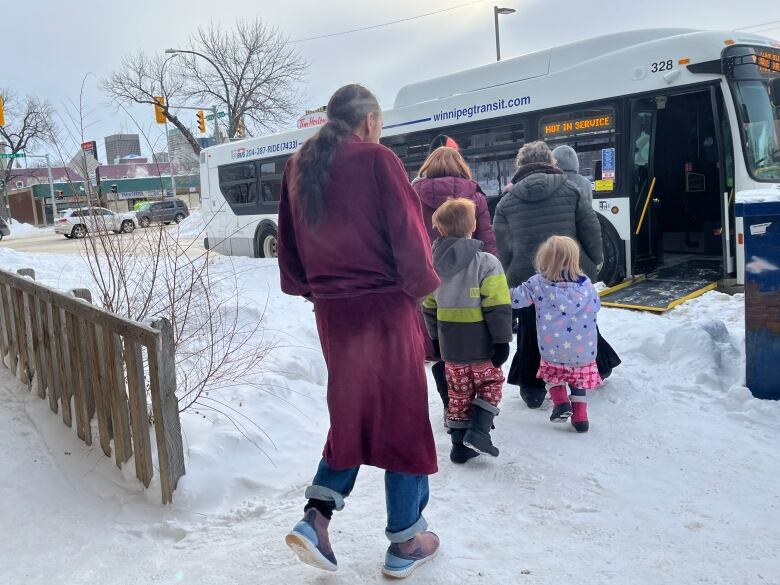 People in housecoats and pyjamas board a Winnipeg Transit bus.