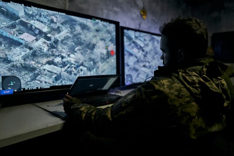 A man in military garb watches a screen.