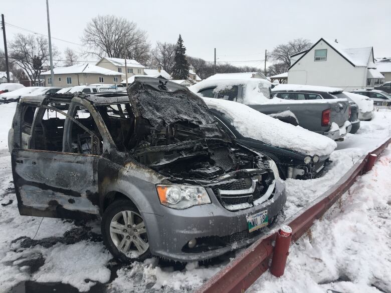 A burned out silver van is parked in a snowy parking lot