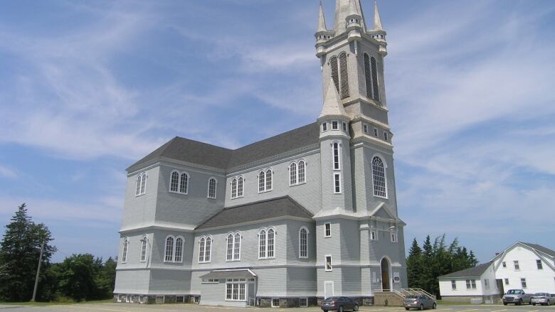 A grey wooden church is shown with the large tower on the right against a blue sky background in Digby County, Nova Scotia.