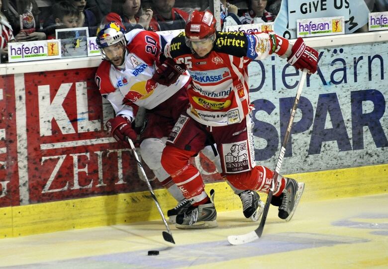 Two hockey players wearing red and white fight for a puck at a game in Austria in 2009.