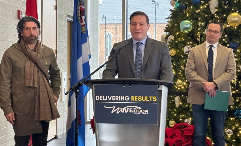 Three men stand at a podium at city hall. 