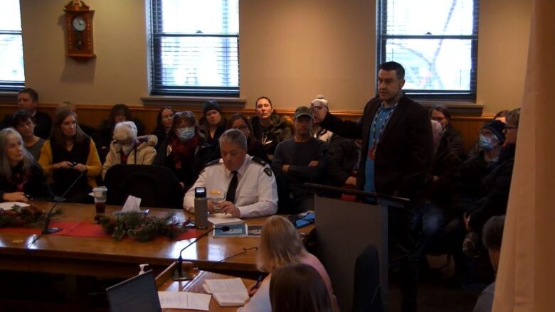 A man stands at a microphone to speak during a public city council meeting