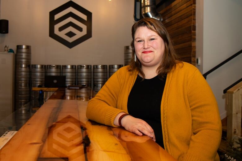 A woman sits smiling at a wooden bar.