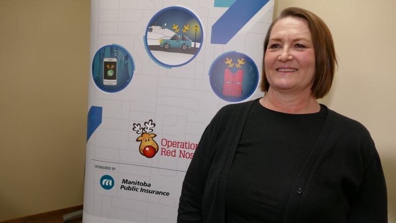 A woman with short, brown hair smiles as she stands in front of an Operation Red Nose banner. 