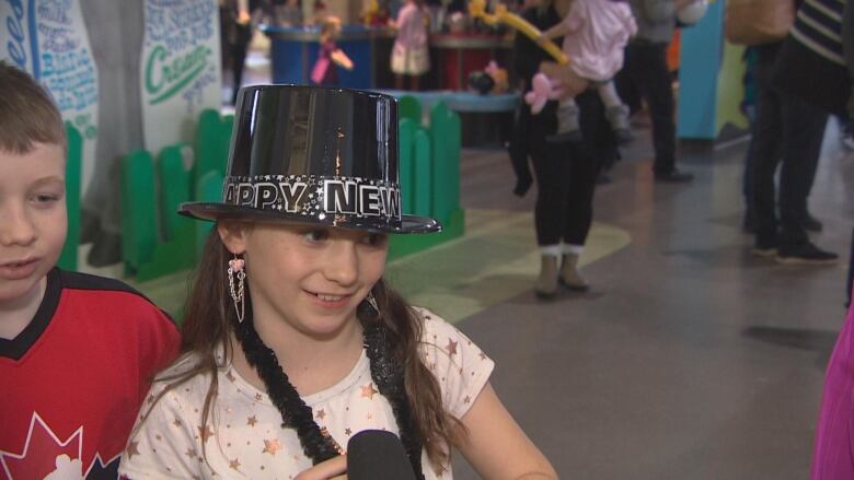 A young girl wears a black plastic top hat.