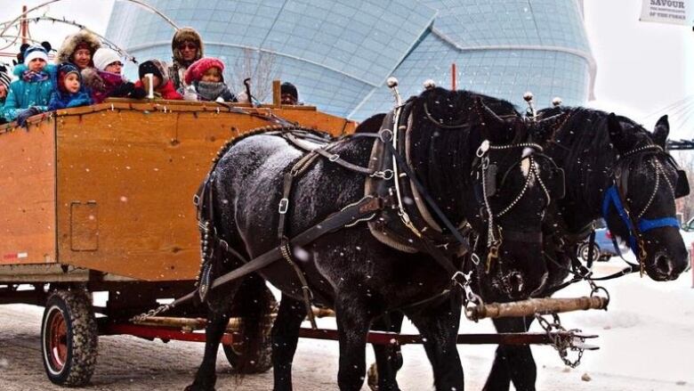 Two horses pull a wagon with children and adults on board.